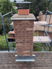 Brick chimney with metal cap on a roof with scaffolding in the background
