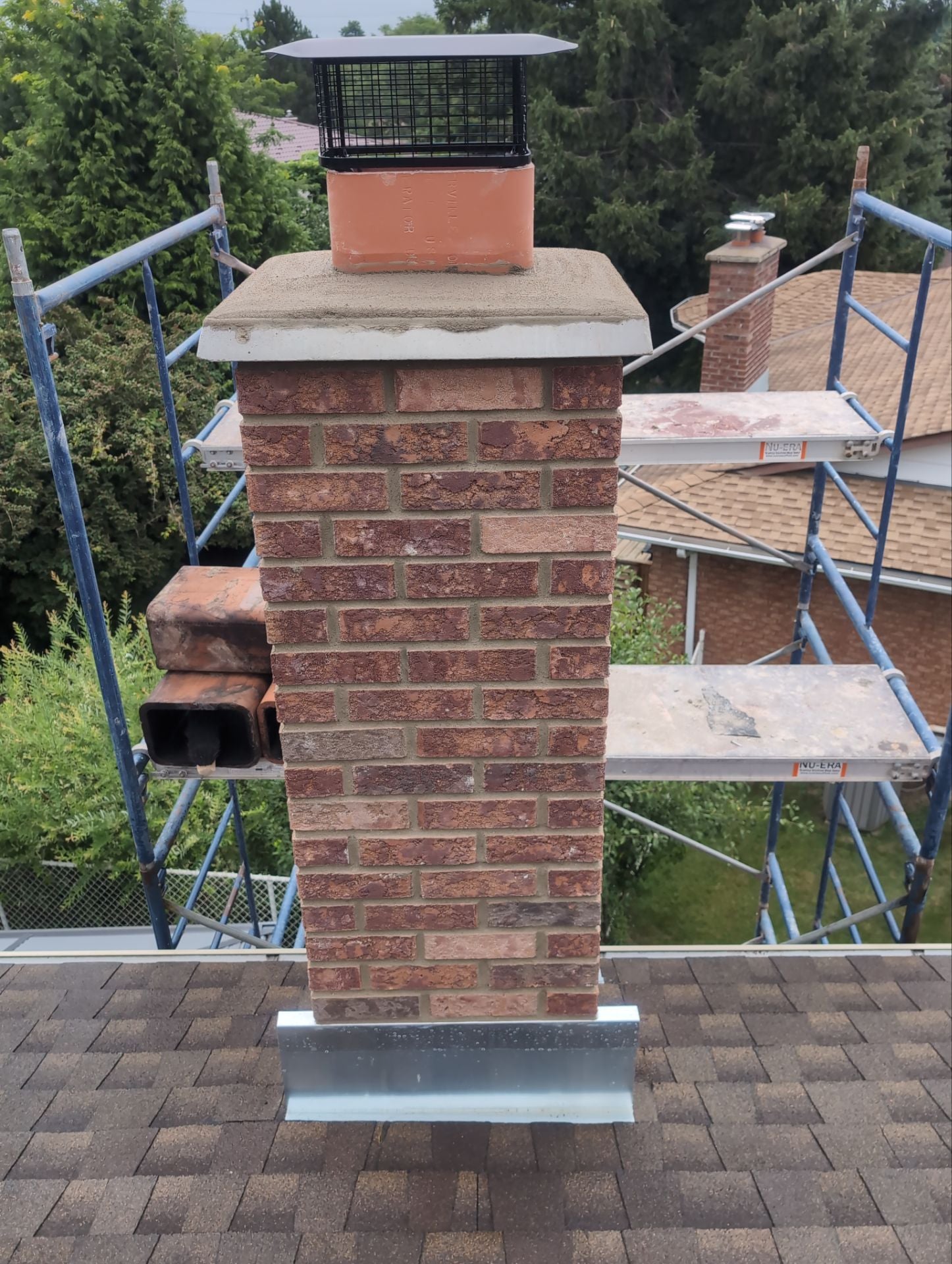 Brick chimney with metal cap on a roof with scaffolding in the background