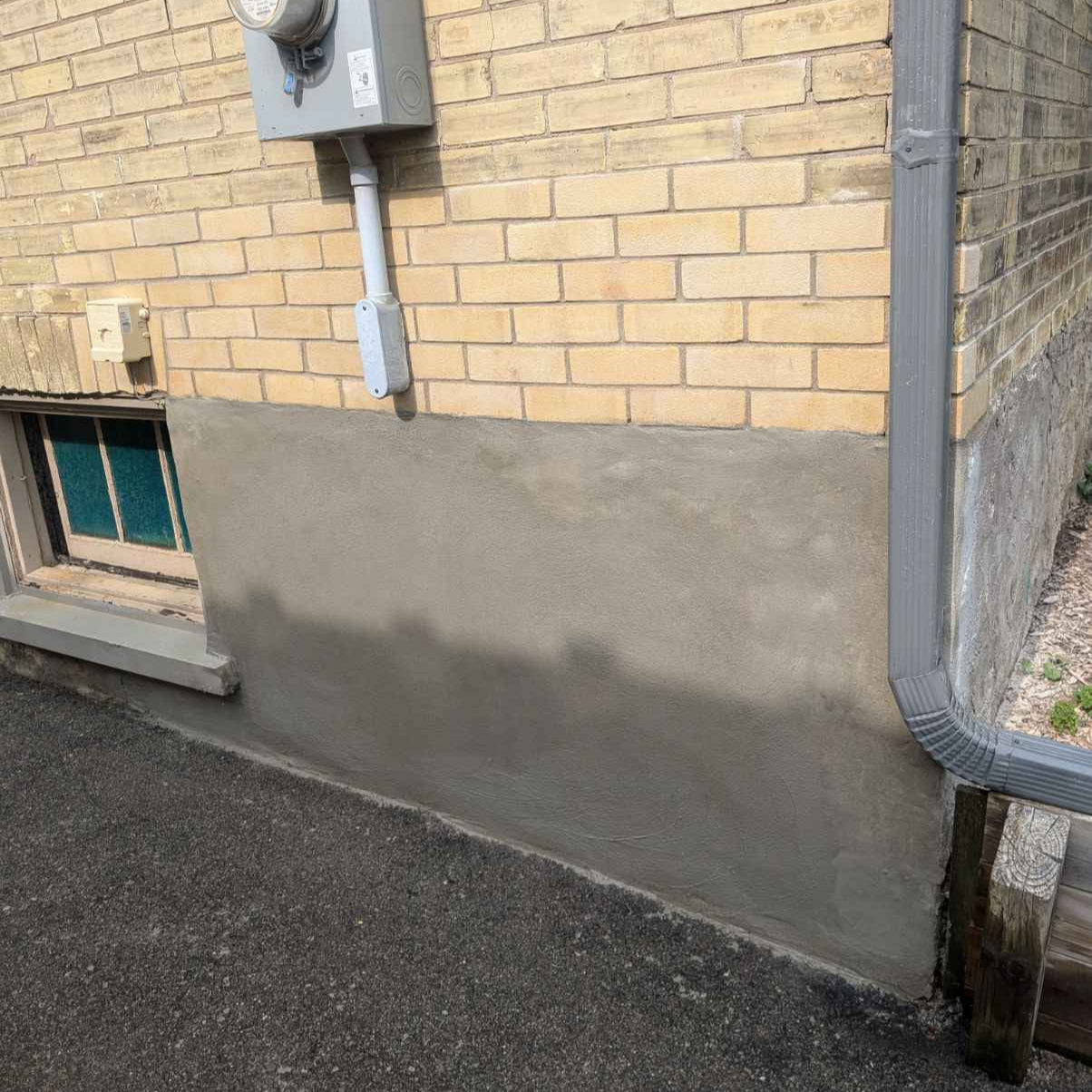Concrete foundation against a brick wall with a window and electrical box.