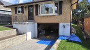 House exterior with a garage door open, covered by blue tarp, and a small deck area.
