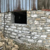 Durable stone foundation wall featuring a basement window opening for ventilation and light in rustic building construction