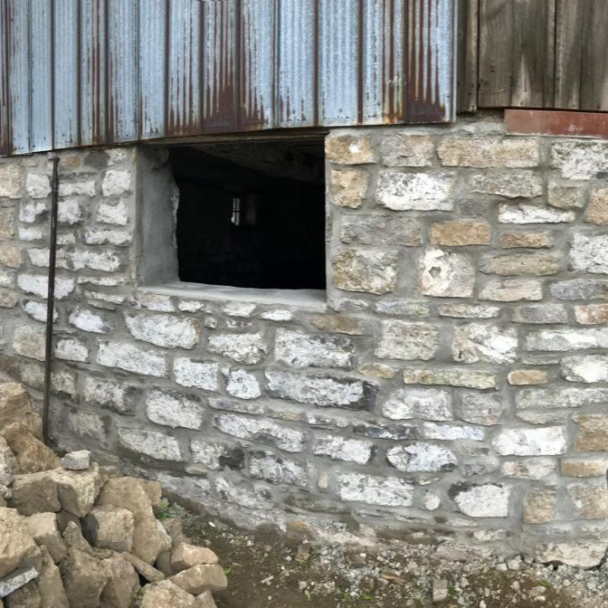 Durable stone foundation wall featuring a basement window opening for ventilation and light in rustic building construction