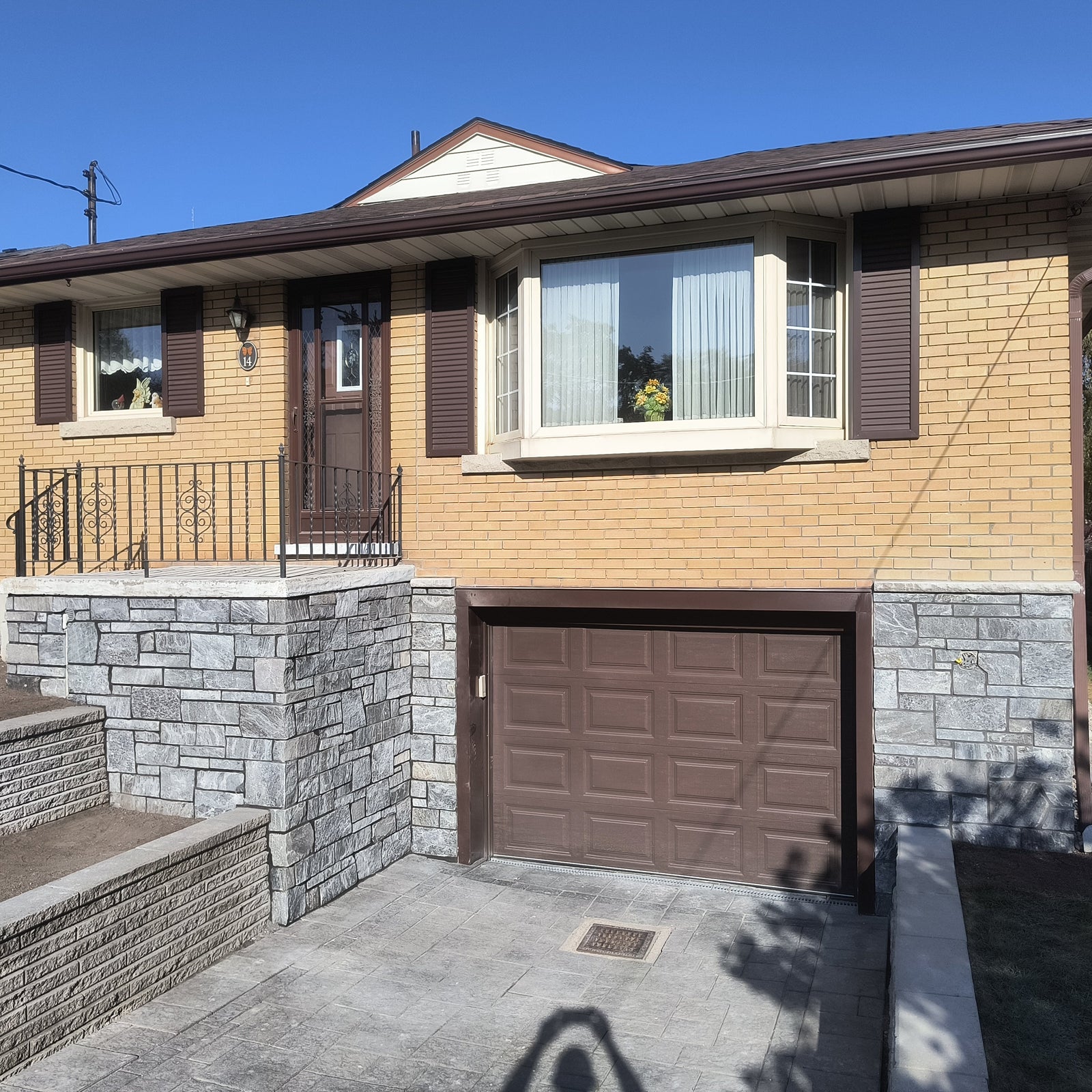 Two-story house with a garage door, stone foundation, and clear blue sky.