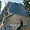 Two workers on ladders applying siding to a house exterior.