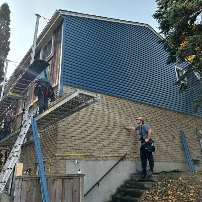 Two workers on ladders applying siding to a house exterior.