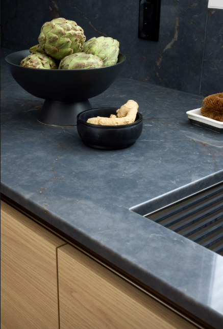 Bowl of artichokes and ginger on a blue countertop with wooden cabinets.