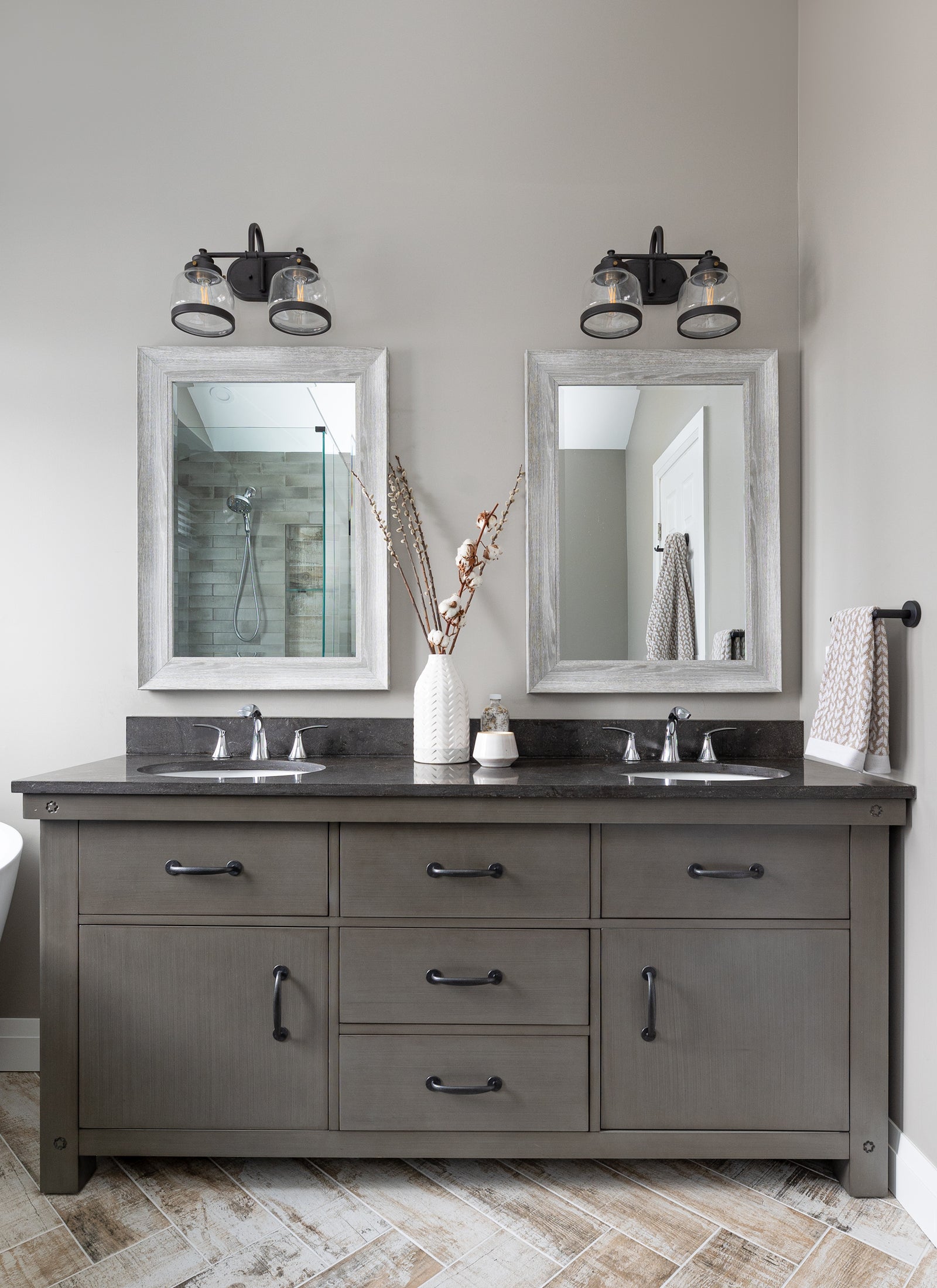 Bathroom vanity with two mirrors, lights, and decorative items on a neutral wall.