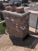 Brick chimney on a roof with three decorative pots on top, in a residential area.