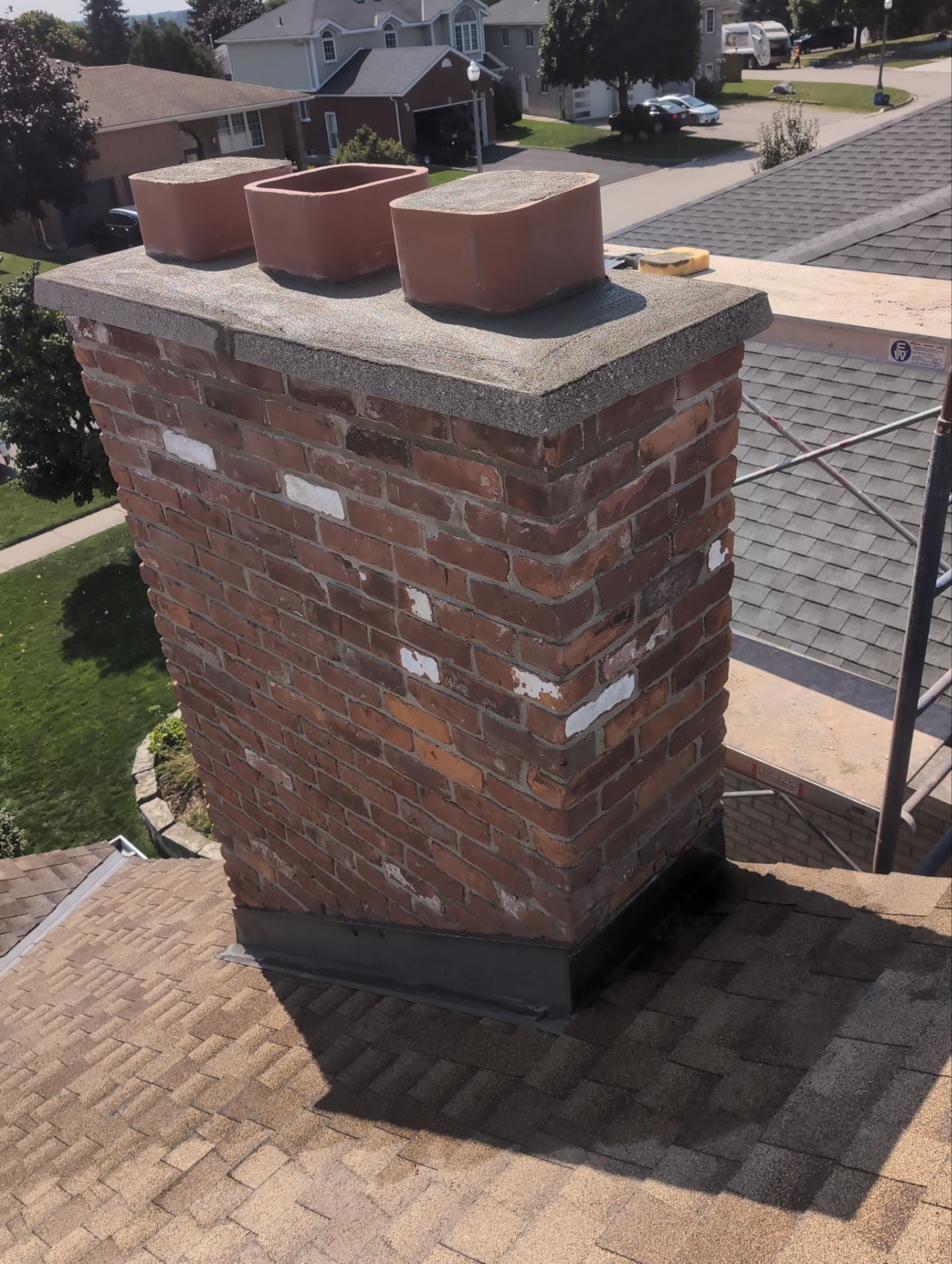 Brick chimney on a roof with three decorative pots on top, in a residential area.
