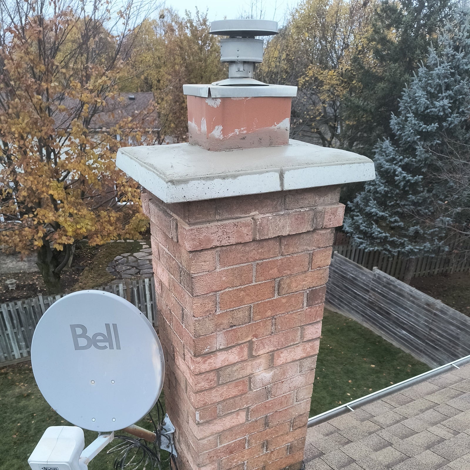 Brick chimney with a satellite dish labeled 'Bell' on a residential roof.