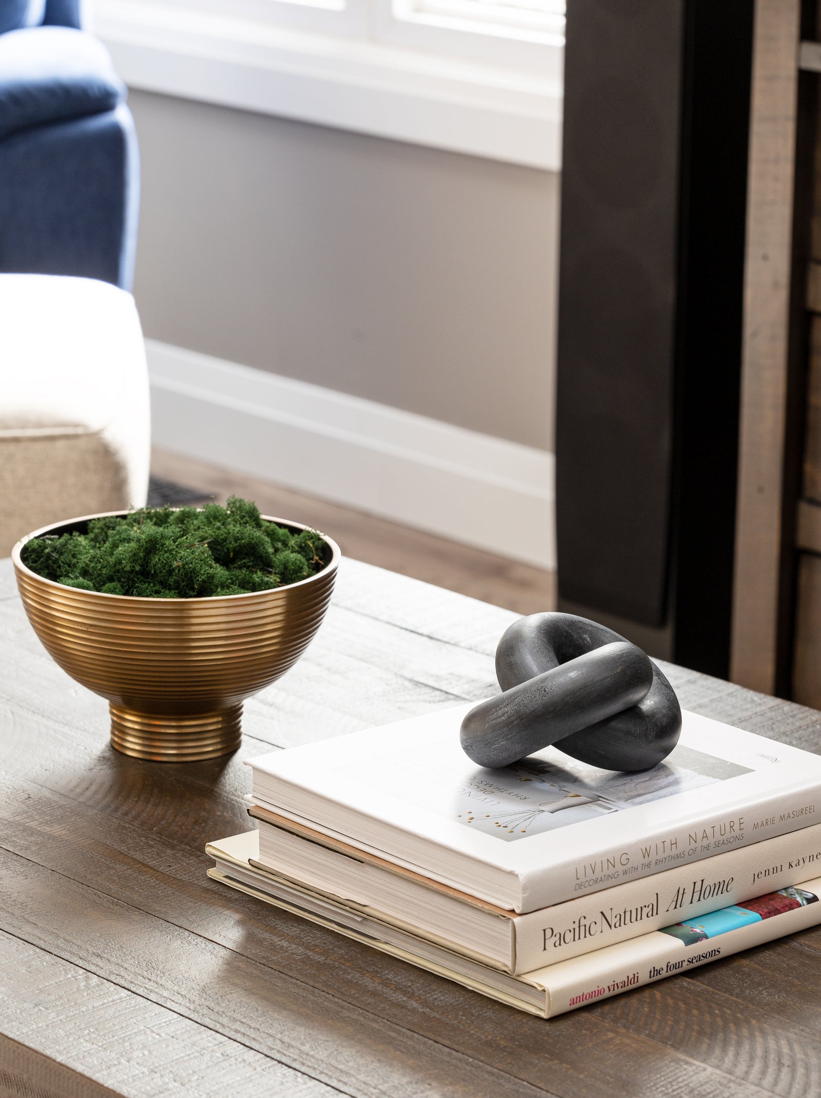 Decorative items including a gold bowl with greenery, a black abstract sculpture, and books on a wooden surface.