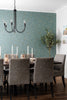 Dining room with a teal patterned wall, chandelier, and gray chairs.