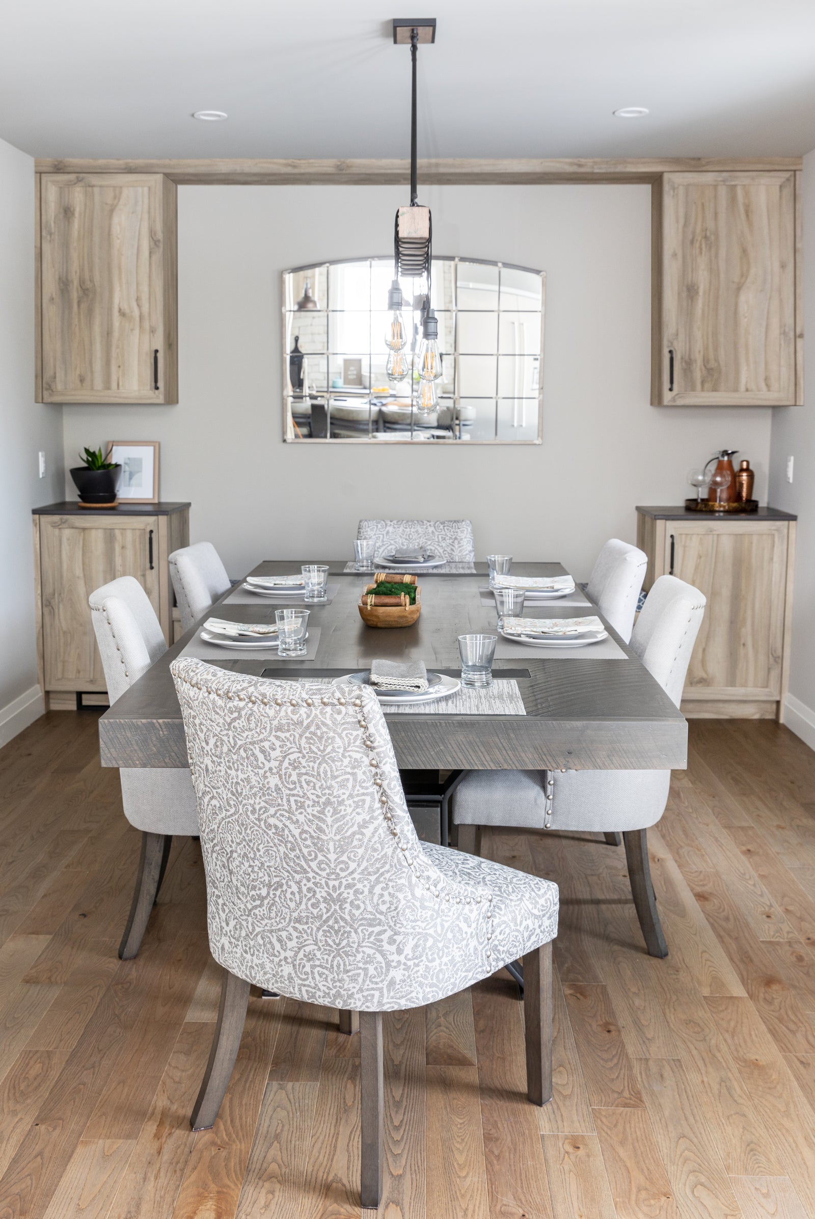 Dining room with a gray table and patterned chairs, wooden cabinets, and a mirror on the wall.