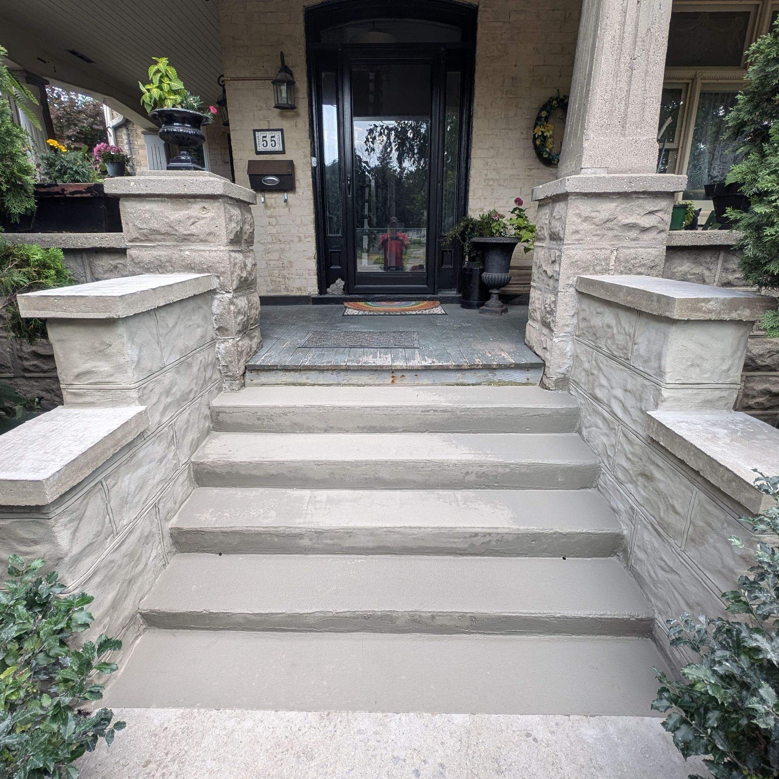 Front steps leading to a house with a black door and stone porch.