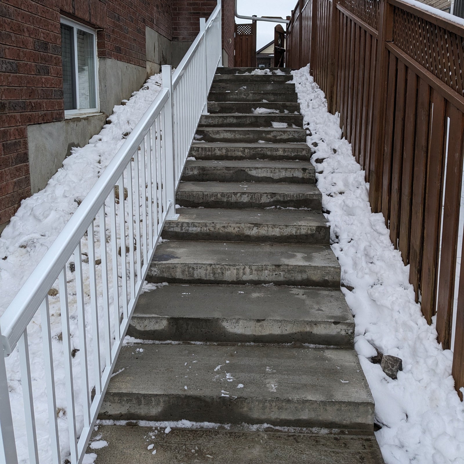Snow-covered staircase leading up to a building with a white railing on one side.