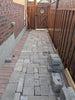 Paver pathway under construction with bricks and a wooden gate in the background.