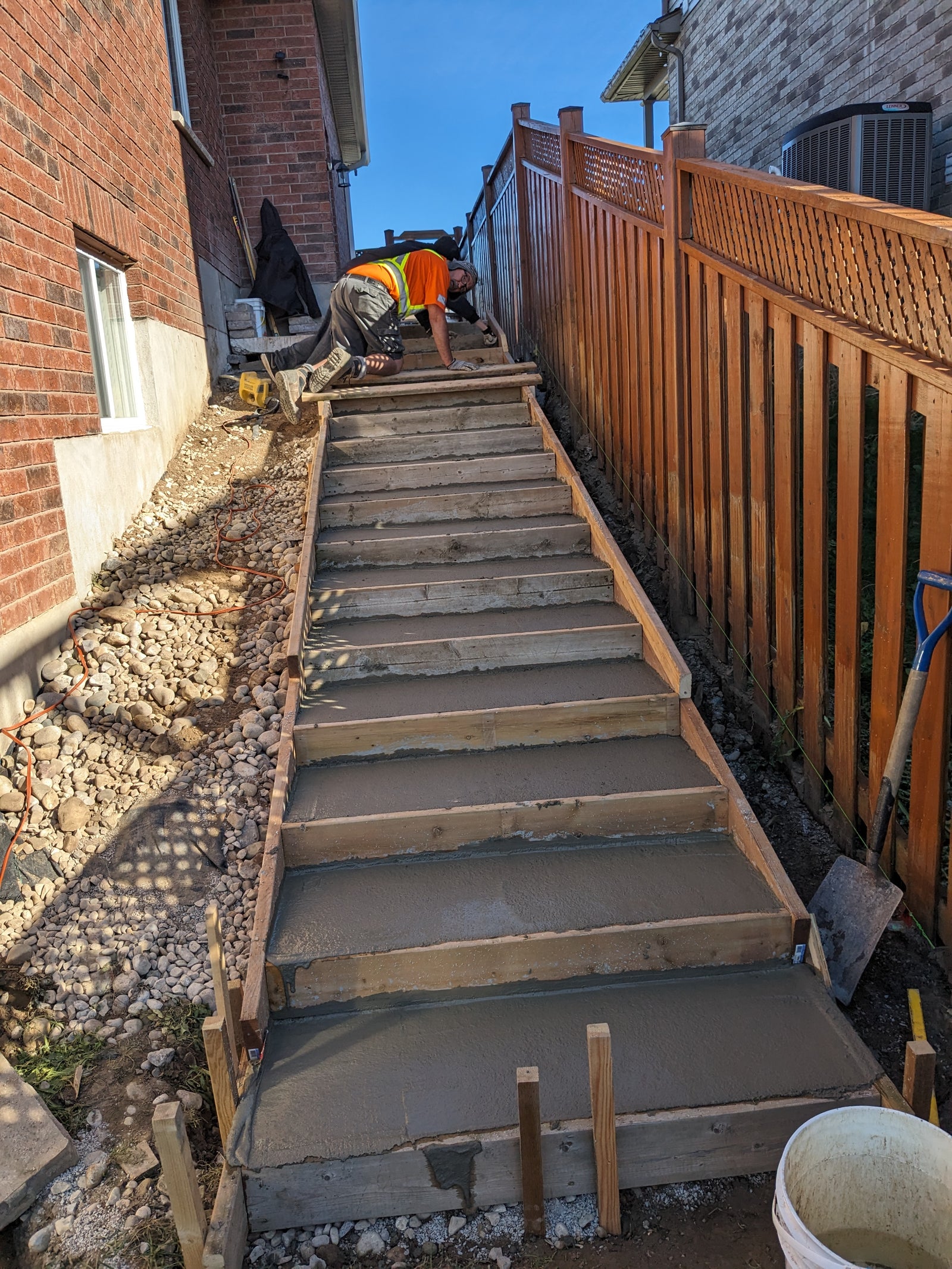 Construction of concrete steps with a worker in an orange vest on a residential property.
