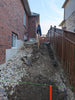 Backyard construction site with excavation and foundational work, featuring a wooden fence and brick house.
