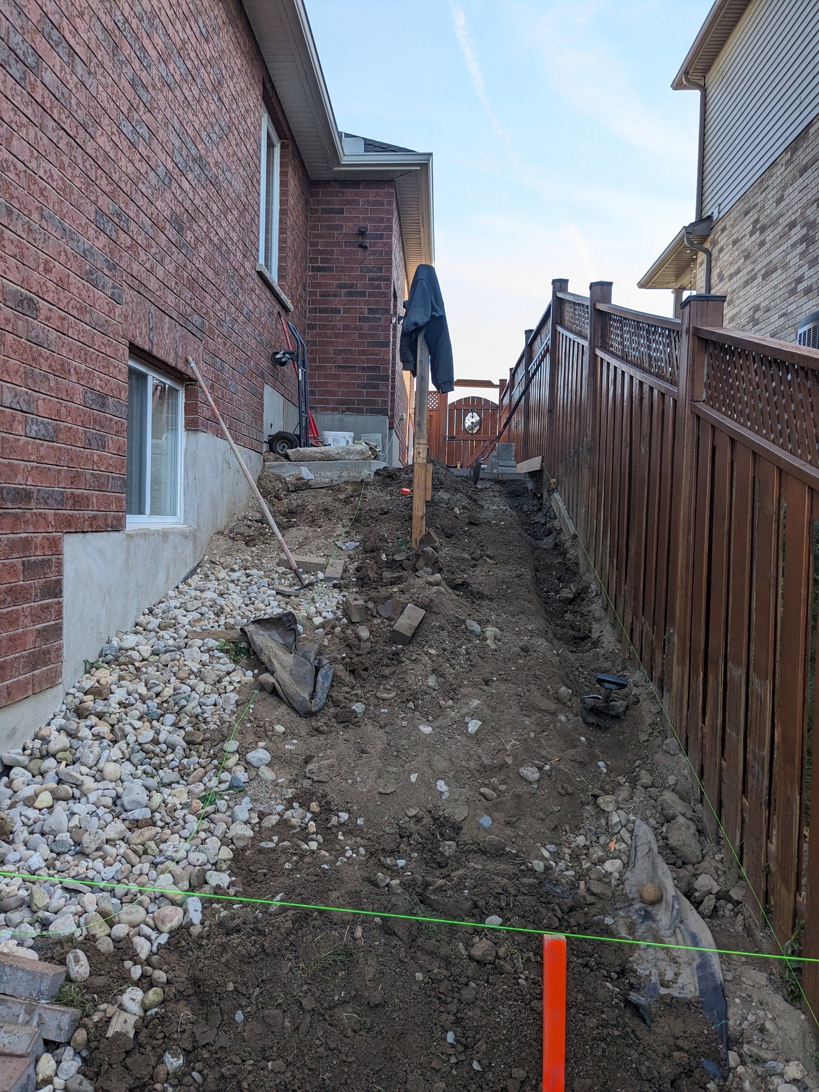 Backyard construction site with excavation and foundational work, featuring a wooden fence and brick house.