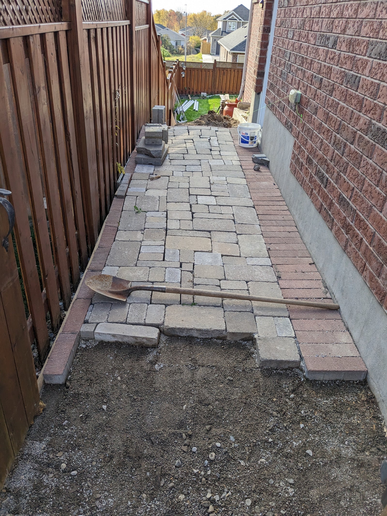 Paving stones being laid out on a gravel surface next to a wooden fence and brick wall.