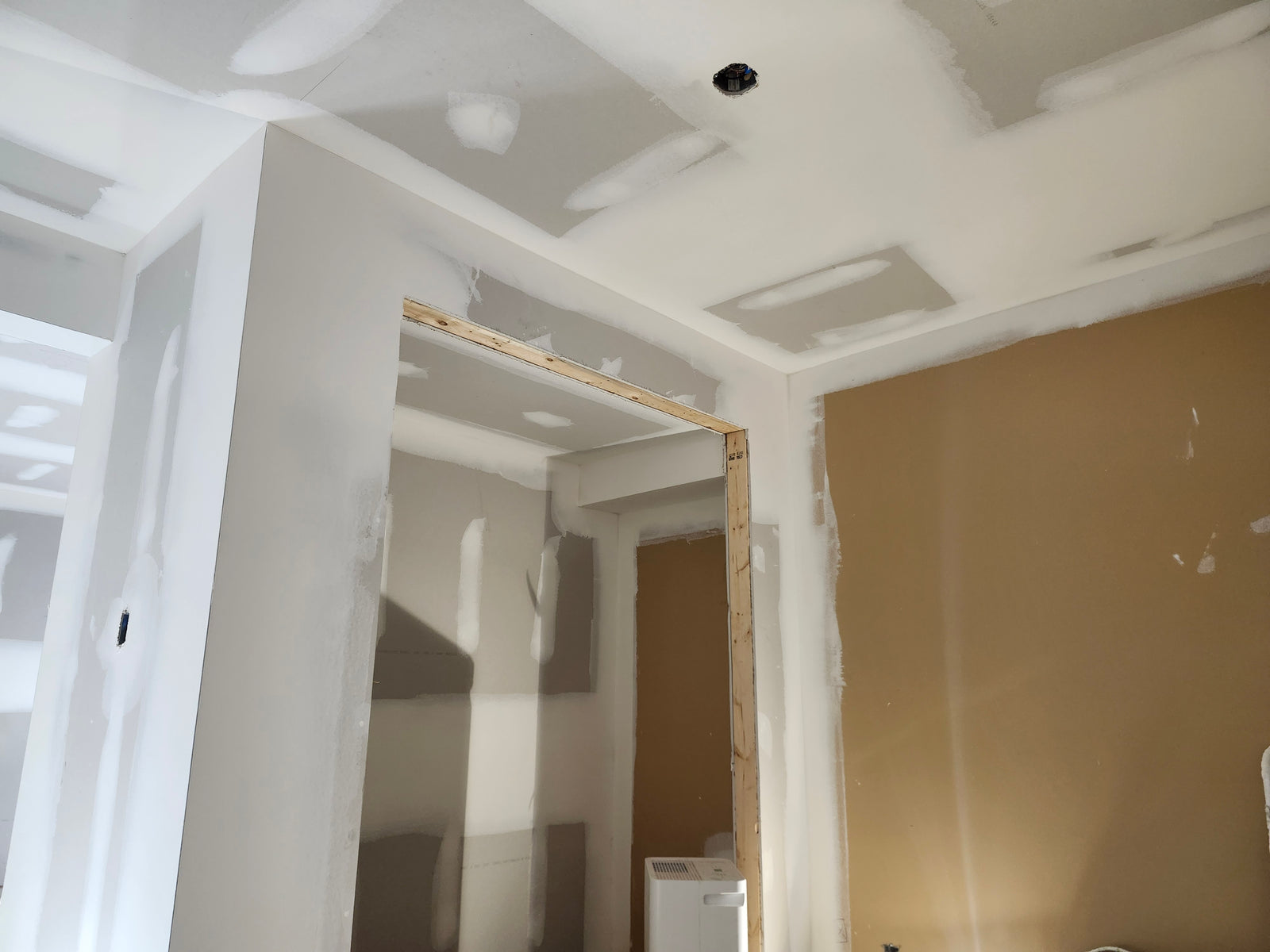 Interior construction scene with drywall in various stages of finishing, exposed door frames, and electrical rough-in installations visible