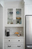 Kitchen interior with white cabinets, refrigerator, and countertop with a coffee maker and bread.
