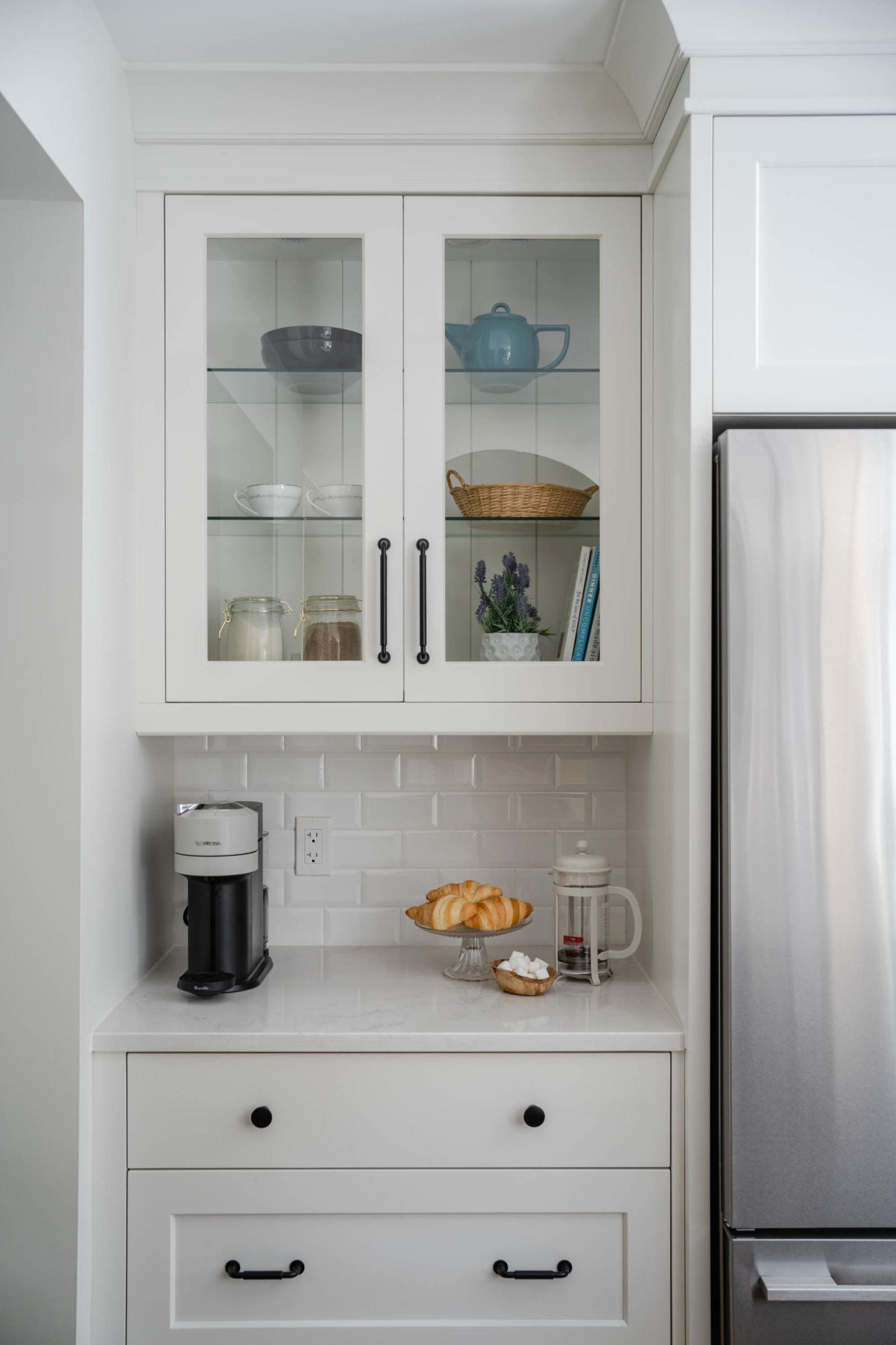 Kitchen interior with white cabinets, refrigerator, and countertop with a coffee maker and bread.