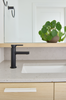 Modern kitchen with black faucet, white sink, and green plant on wooden shelf.