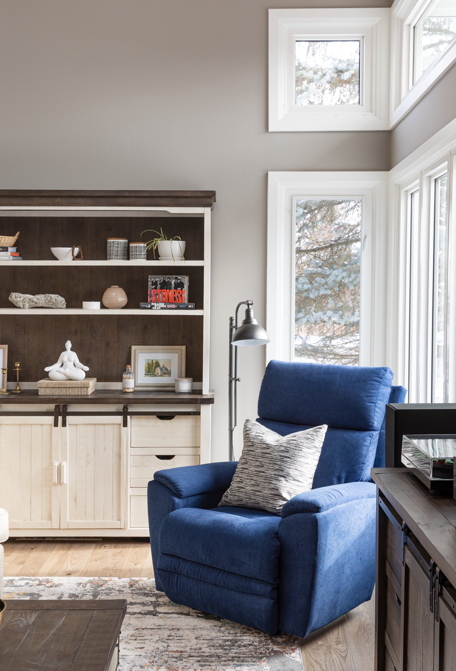 Blue armchair in a living room with a bookshelf and windows.