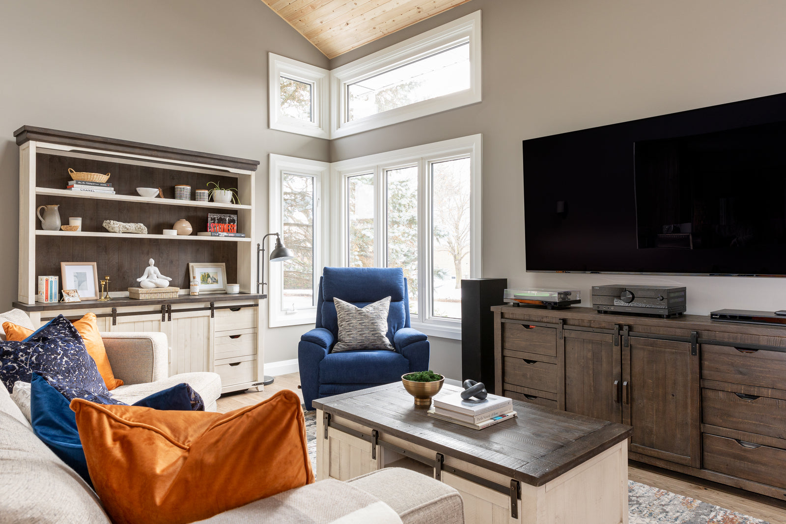 Living room with a blue armchair, orange pillow, and a large TV.