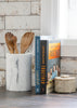 Marble utensil holder with wooden spoons next to cookbooks on a wooden surface.