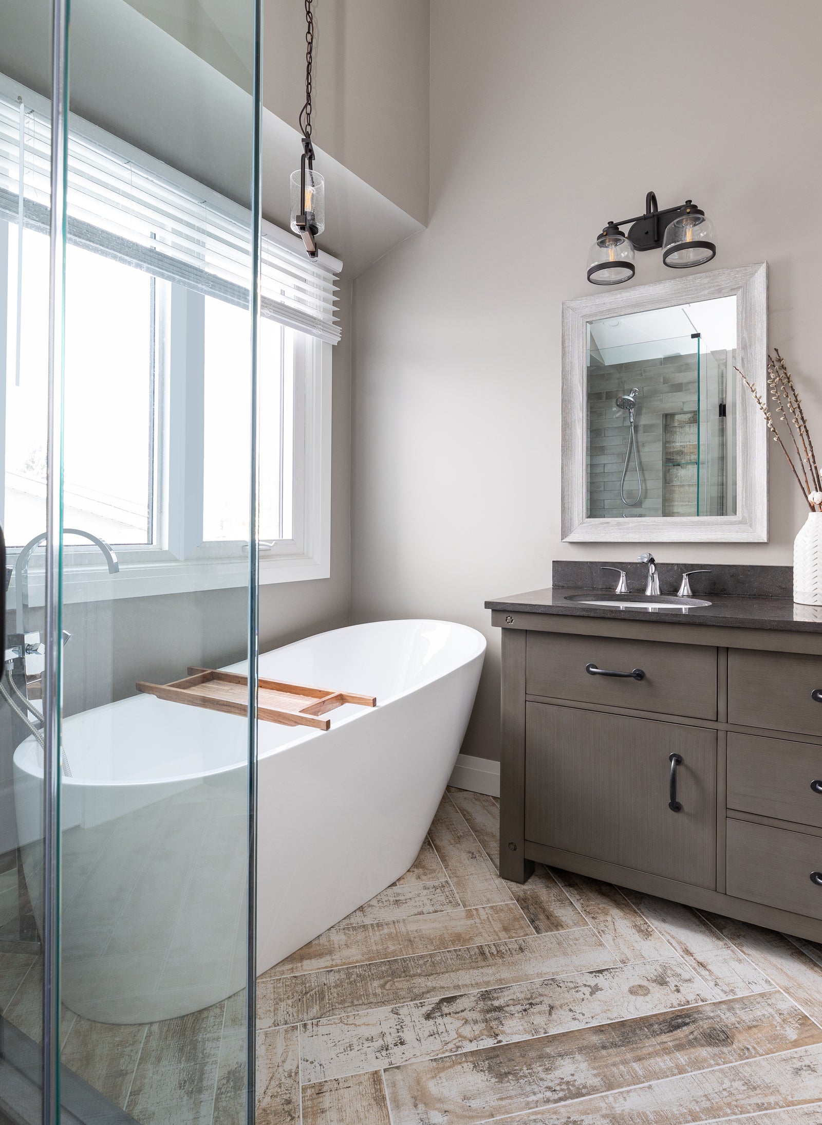 Modern bathroom with freestanding bathtub, wooden floor, and gray vanity.