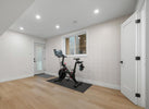 Home gym with a stationary bike in a room with light wood flooring and white walls.