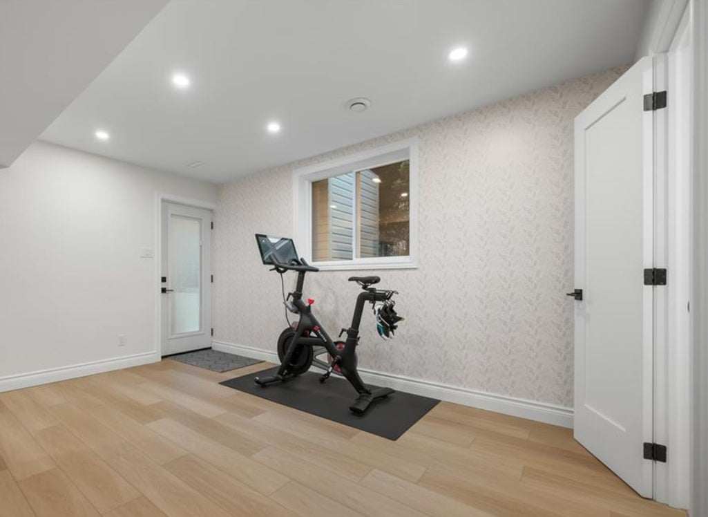 Home gym with a stationary bike in a room with light wood flooring and white walls.
