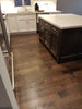 Modern kitchen with dark hardwood flooring, white cabinets, stainless steel appliances, and a large dark island with quartz countertop