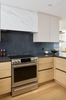 Modern kitchen with stainless steel oven, marble backsplash, and wooden cabinets.