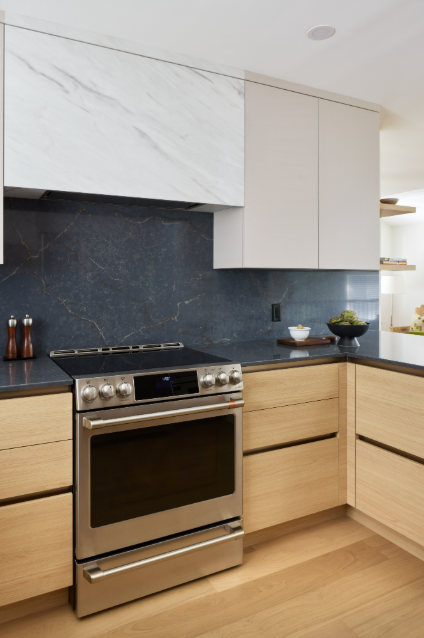 Modern kitchen with stainless steel oven, marble backsplash, and wooden cabinets.