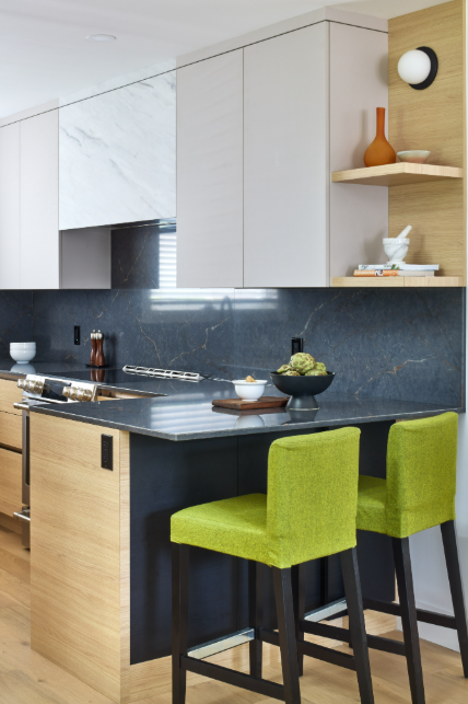 Modern kitchen with dark marble countertop, white cabinets, and green stools.