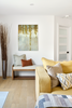 Modern living room with yellow sofa, wooden bench, and decorative wall art.