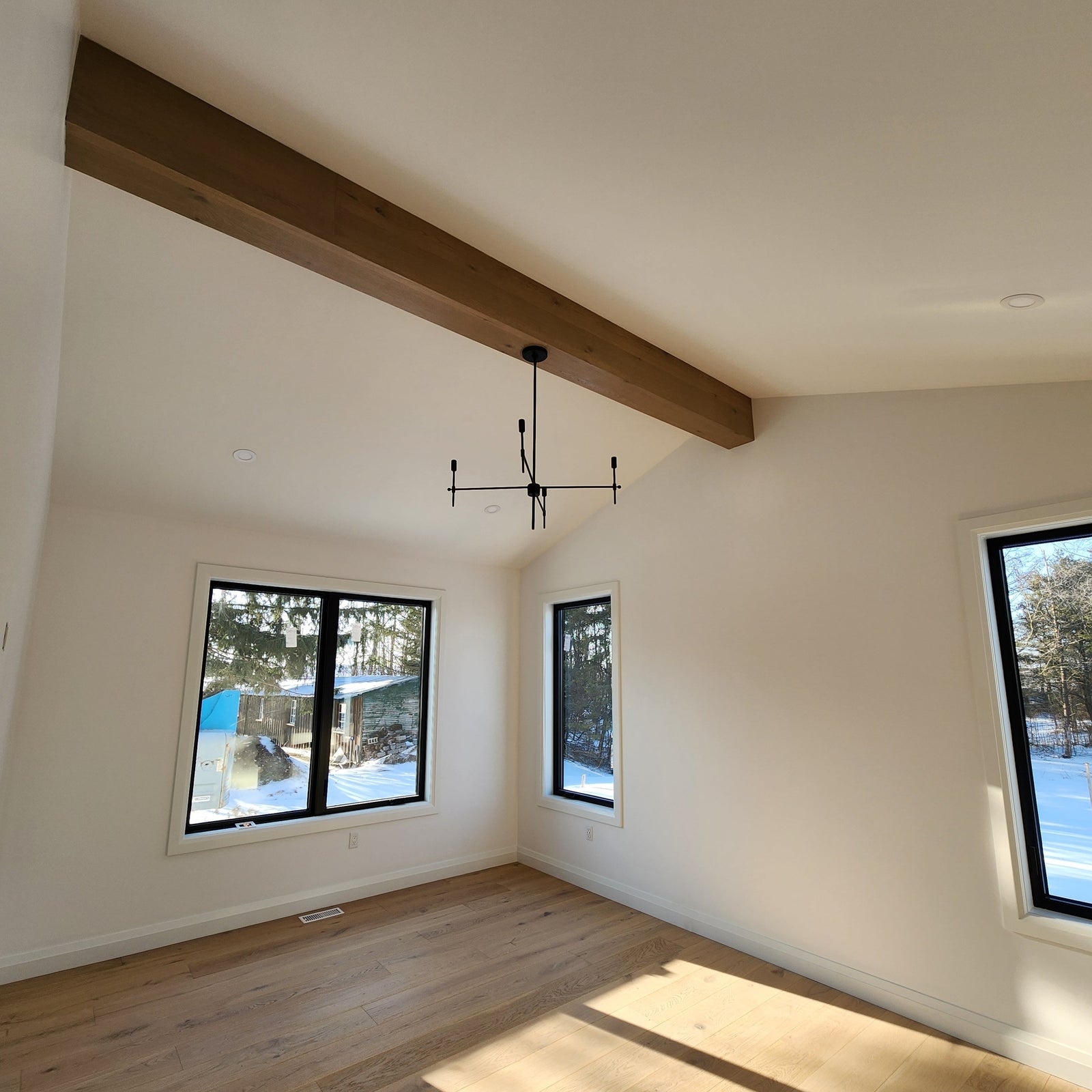 Modern room with wooden beams, large windows, and light wood flooring.