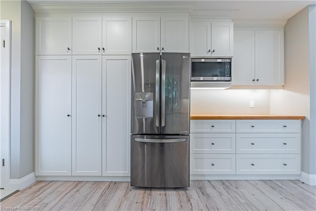 Modern kitchen with white shaker cabinets, stainless steel French door refrigerator, built-in microwave, and wood countertop in residential home