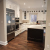 A newly renovated kitchen featuring white cabinets, a stainless steel refrigerator, oven and range, a dark island with a granite-like countertop, and a tile backsplash.