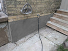 Outdoor shower with hose attached to a brick wall next to wooden steps.