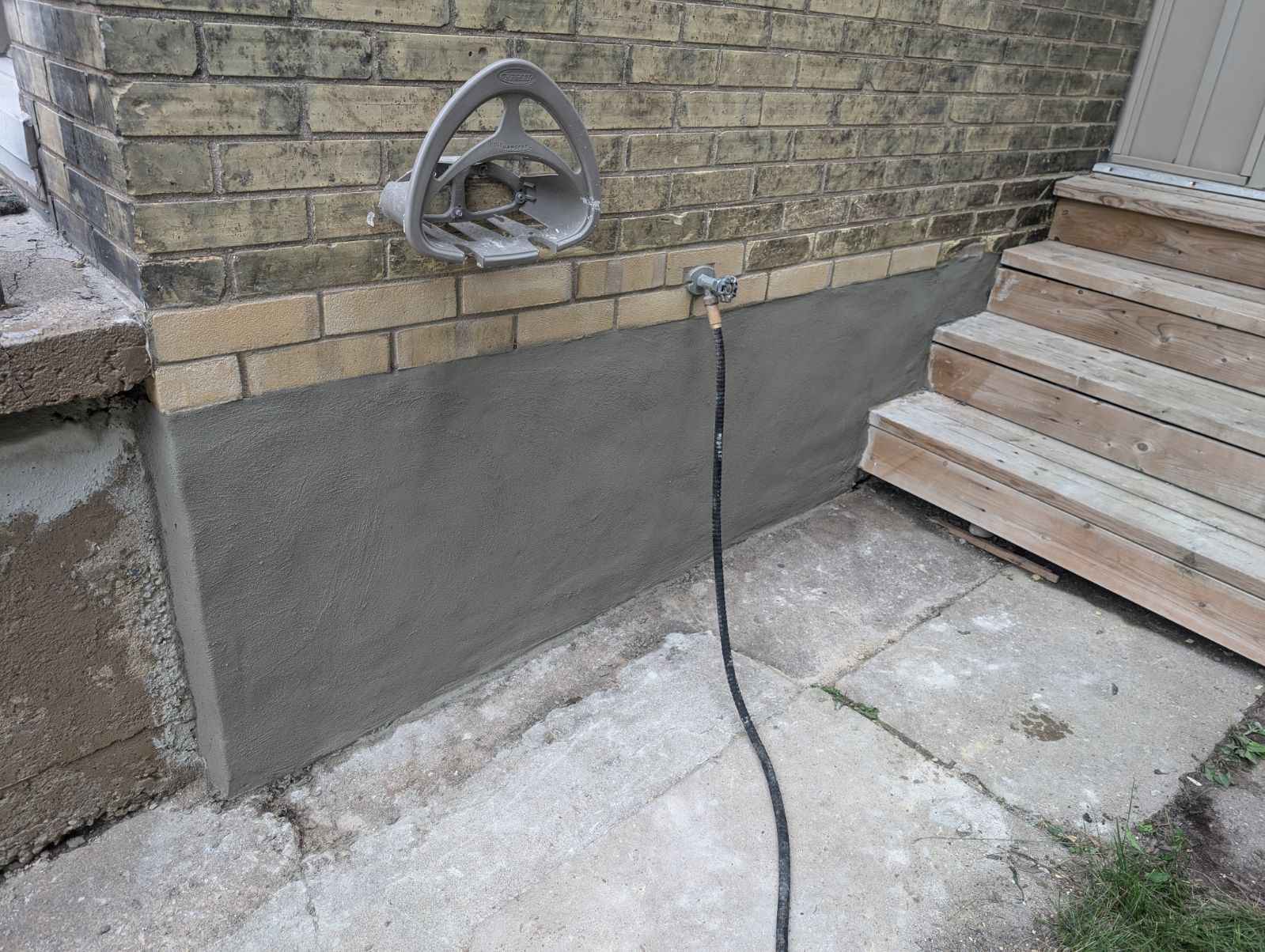 Outdoor shower with hose attached to a brick wall next to wooden steps.