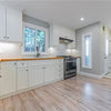 A renovated kitchen featuring white cabinets, wood countertops, stainless steel appliances, and a bright window.