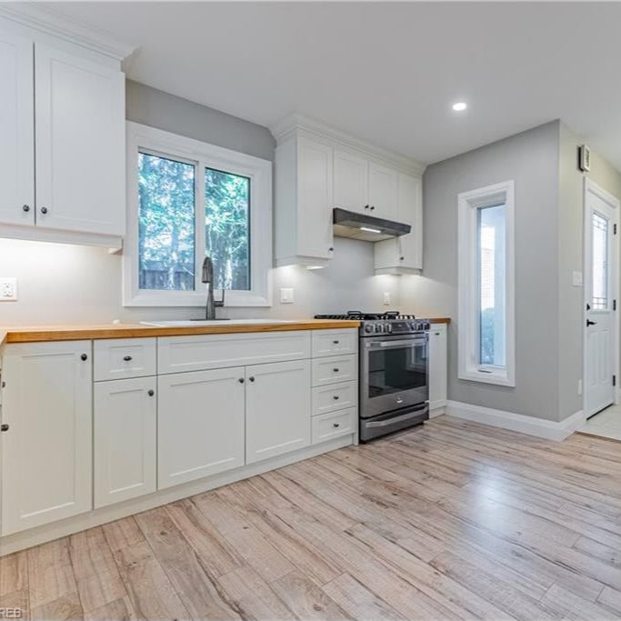 A renovated kitchen featuring white cabinets, wood countertops, stainless steel appliances, and a bright window.