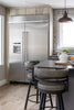 Modern kitchen with stainless steel refrigerator, bar stools, and a dining table.