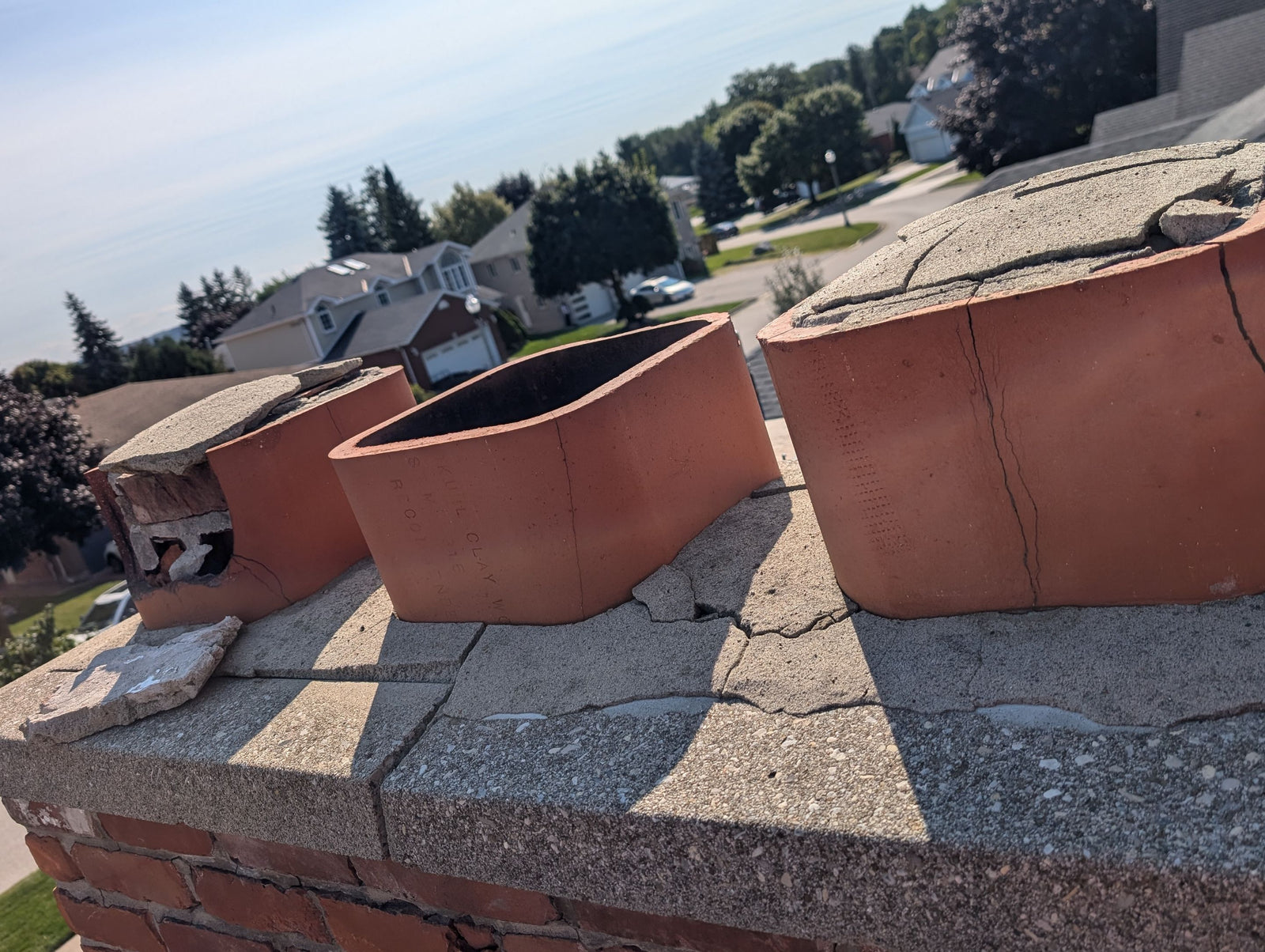 Three terracotta roof tiles on a roof with a suburban neighborhood in the background.