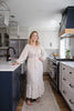 Woman standing in a modern kitchen wearing a long, light-colored dress.