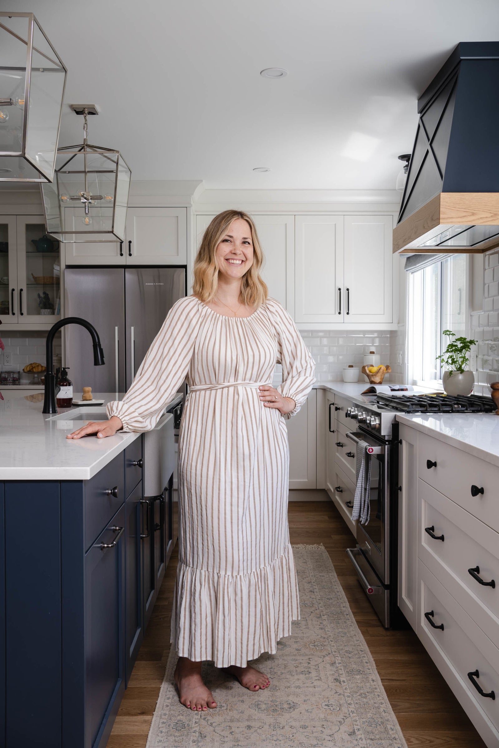 Woman standing in a modern kitchen wearing a long, light-colored dress.